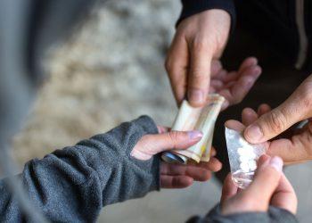 Close-up of hands exchanging cash for a small transparent bag of white pills.