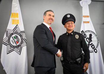 Two men shake hands in front of security agency banners during a formal ceremony—the suited official and a police officer in uniform smile for the photo.