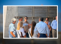 Group of professionals standing in a circle outside, discussing near a concrete wall backdrop in sunlight.