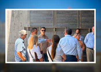Group of professionals standing in a circle outside, discussing near a concrete wall backdrop in sunlight.
