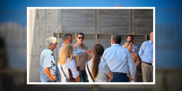 Group of professionals standing in a circle outside, discussing near a concrete wall backdrop in sunlight.