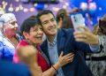 Man in a blue suit takes a smiling selfie with an elderly woman in red at a festive event.